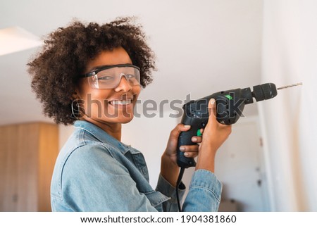 Afro woman drilling wall with electric drill.