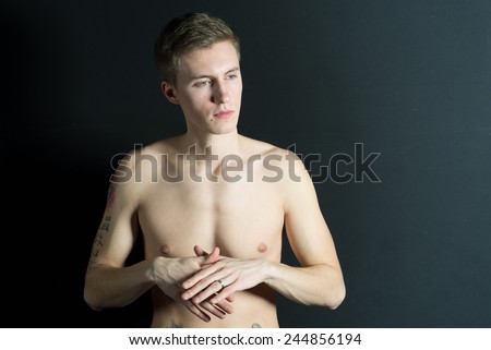 Young thin man, naked torso on black background