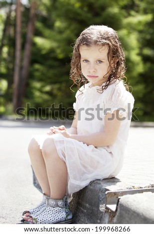 the little girl is sad sitting on bordure with wet hair