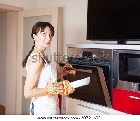 a woman in an apron and gloves prepares in the oven