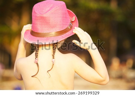 little girl back on the beach in a pink hat with braids