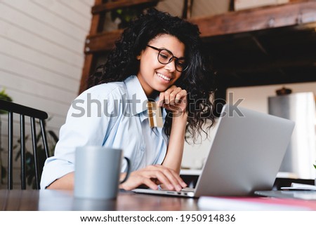 Beautiful young african-american woman buying online on laptop at home. African American woman look at laptop screen shopping online with credit card for payment. Happy young girl buy purchas.