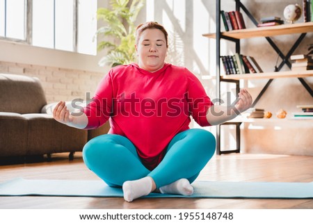 Plump obese caucasian fat woman meditating in sporty outfit at home. Fat woman sitting and relaxing in lotus position. Chubby woman doing yoga at home for losing weight Сток-фото © 