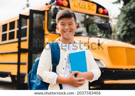 Asian korean japanese chinese schoolboy pupil student going back to school after summer holidays lockdown quarantine holding books and copybooks standing at school yard near bus 商業照片 © 