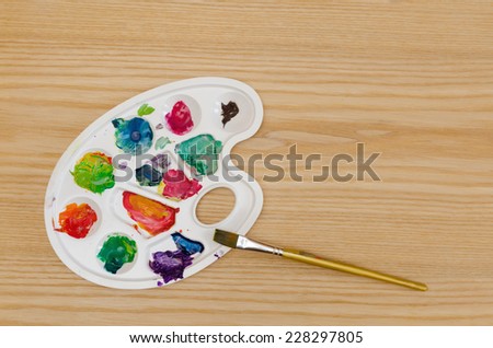palette with smudges of paint and a brush on a wooden table