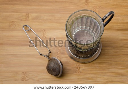 top view of retro tea cup with hot water and a mesh tea infuser on wooden table