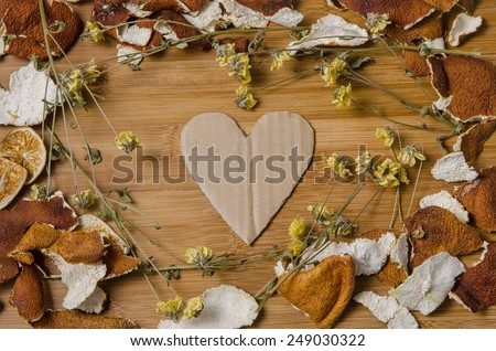 cardboard heart surrounded by a frame of dry citrus peel and withered flowers on a wooden table