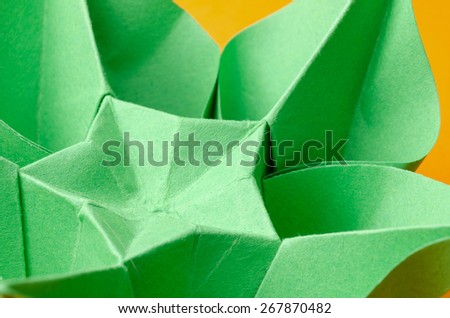 Abstract closeup of a green paper origami flower with star shape in the middle on orange background. Side view.