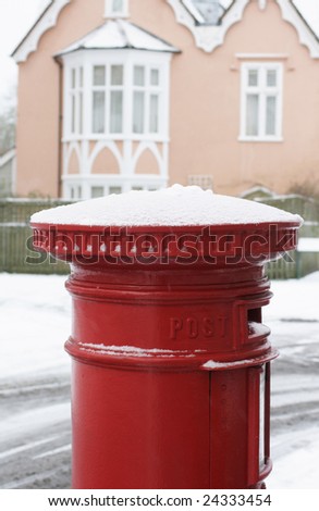 A red pillar box topped with winter snow with a period building to background. located in Salisbury, Wiltshire, England.