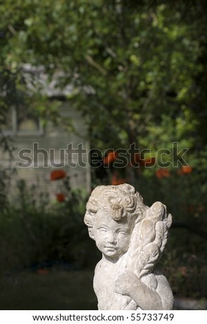A stone carved garden statue ornament of a cherub in a rural garden setting. Soft focused greenery and red poppies to background.