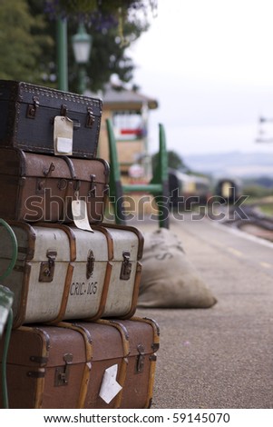 A set of labeled period luggage consisiting of old leather cases, set on a trolly on the platform of a retro railway station.