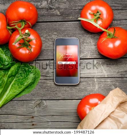 Cooking recipes on smart phone with vegetables on background.