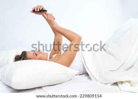 Young woman in looking at mobile phone while lying in bed