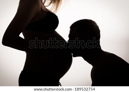 Silhouette profile of a man kissing pregnant belly of his woman.Family, love and care concept.