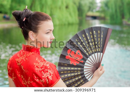 young Asian girl walking in national dress with a fan near the river