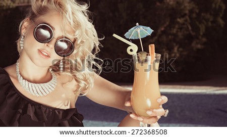 Fashion beautiful woman sunbathing on a chaise lounge with fresh orange juice in luxury pool. Vogue style