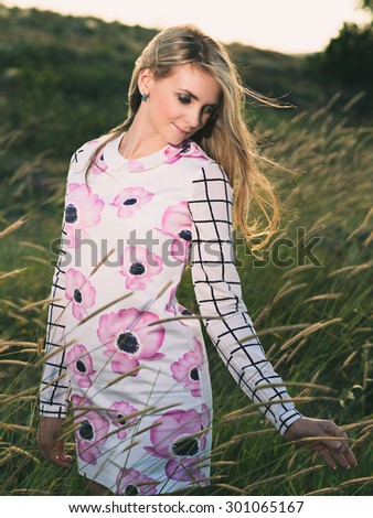 portrait of the attractive, slender, beautiful young Caucasian  blonde girl outdoor. Beautiful modern woman  with the long developing fair hair in a loose dress. dressy style. snub nose