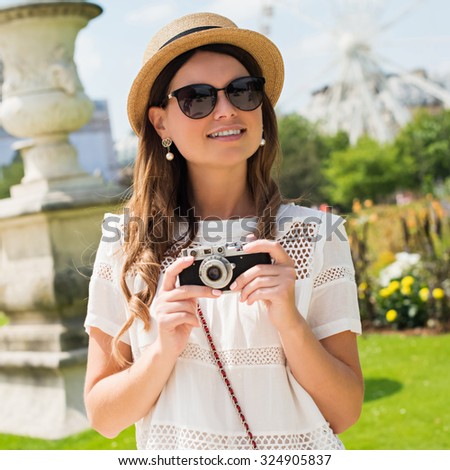 young attractive woman in hat, white dress, red bag and retro camera poses against Paris. Fashion and city style.