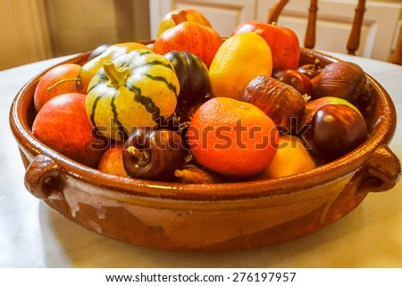 Vintage looking Many different fruits and vegetables in a bowl including oranges and chestnuts and pumpkins