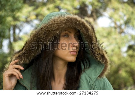 A beautiful woman raises her fur-lined parka to look into the distance.