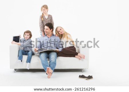 All family sitting on a white sofa on a white background and reading a book.