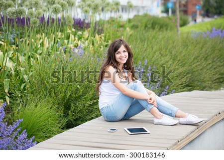 Young beautiful woman in the park with gadgets outdoors in a park
