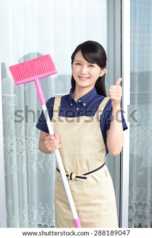 Smiling young woman with a broom sweeping the balcony
