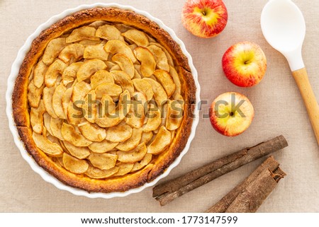 Homemade baked French apple tart, an open faced apple pie, in a baking white ceramic dish aside Gala red apples, cinnamon sticks and white cooking spoon, all on a natural linen table cloth. Flat lay Stok fotoğraf © 