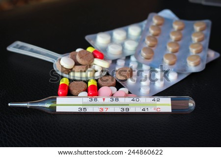 Mercury thermometer shows a temperature of 39 C on the background of tablets