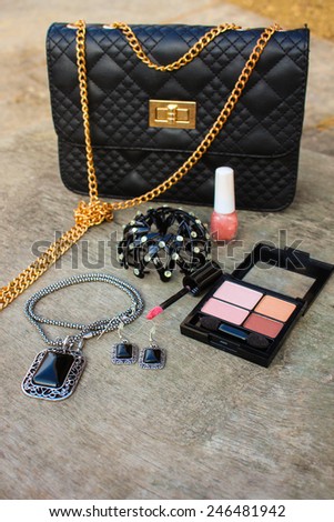 Women's accessories: eyeshadow, lip gloss, nail polish, clip hair, necklace, black handbag