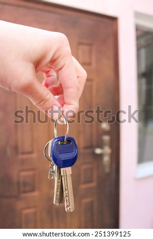 Female hand holding a key on the background of the doors of the house