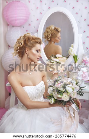 Beautiful bride with  makeup and hairstyle in bedroom.Happy Bride waiting groom. Marriage Wedding day moment. Woman in white dress,perfect skin, blond hair. Wedding decoration. Bride with flowers