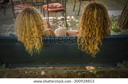 Two girls sitting in the garden on bench from back