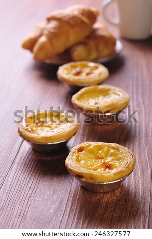 delicious chinese egg tart with croissants, cup of black coffee on wooden background