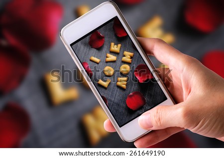 using mobile phone to take photos of Cookies ABC in the form of word I LOVE MOM alphabet with red rose petal on old jean background, Valentines day