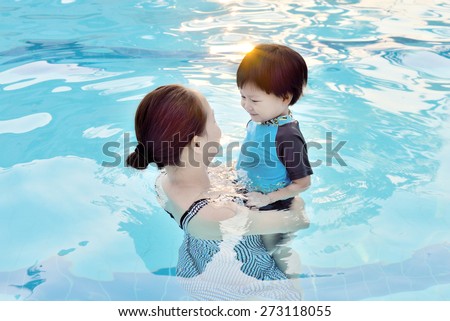 Young mother and her son having fun in a swimming pool