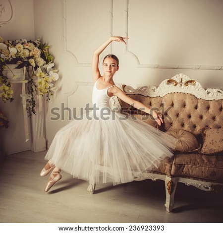 Little ballerina girl in a dress, classical, ballet dance. A girl in a ball gown sitting on sofa classic, white background, white sofa classic.
