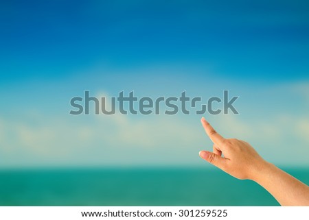 Woman hand pointing on blurred image of blue-sky with clouds on the beach.