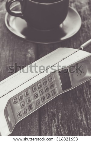 vintage mobile phone with coffee cup on old table (vintage style)