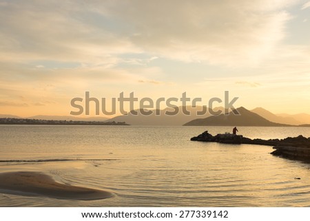 Sunset over the Aegean Sea, with a Person Relaxing on the Backshore and other Aegean Islands in the Background
