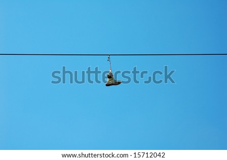 Two sneakers with shoelaces tied to each other thrown on an wire