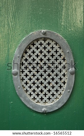 Detail of an old wooden door with a large eye hole covered by a round ornament piece of metal