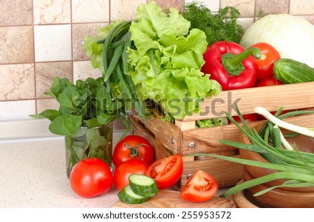 The fresh washed-up vegetables in a wooden box and the cut vegetables on a chopping board against modern kitchen.