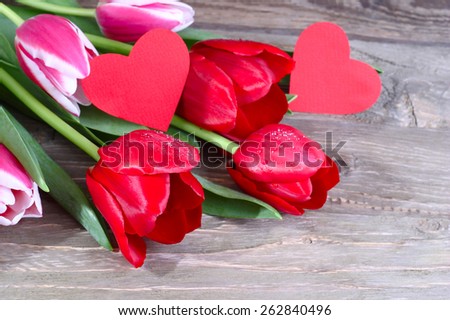 Bouquet of fresh red tulips and two red cardboard hearts on a wooden background.