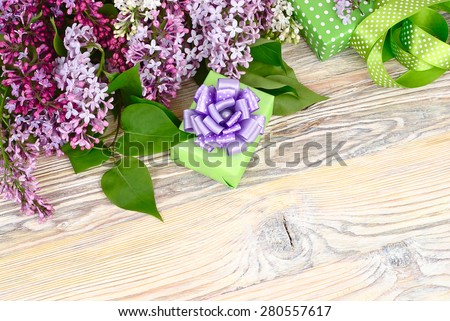 Flower wooden background with a lilac, a gift box and tapes with a place for the text. Top view. A background to the subject \