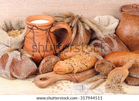 Fresh bread, ears, grain and milk in a jug on a wooden background.