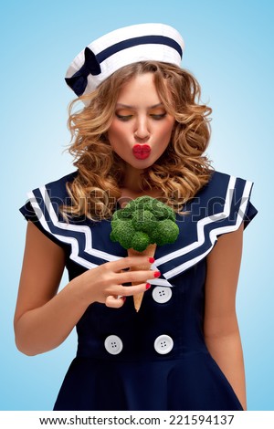Creative retro photo of a fashionable pin-up sailor girl looking surprised with a broccoli ice cream in a waffle cone on blue background.