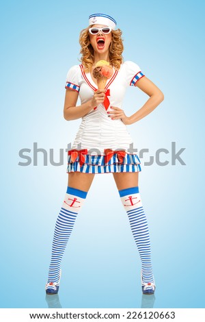 Creative retro photo of a fashionable pin-up sailor girl, holding an ice cream in a waffle cone and screaming on blue background.