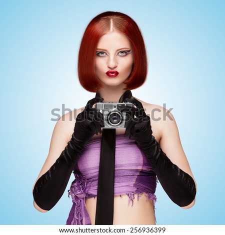 Glamorous girl, vintage vamp style, dressed in a necktie and long gloves, shooting with an old vintage photo camera on blue background.