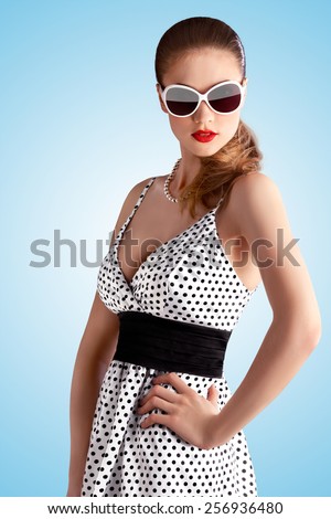 Creative vintage portrait of a beautiful pin-up girl wearing a fashionable retro dress in polka dots on blue background.